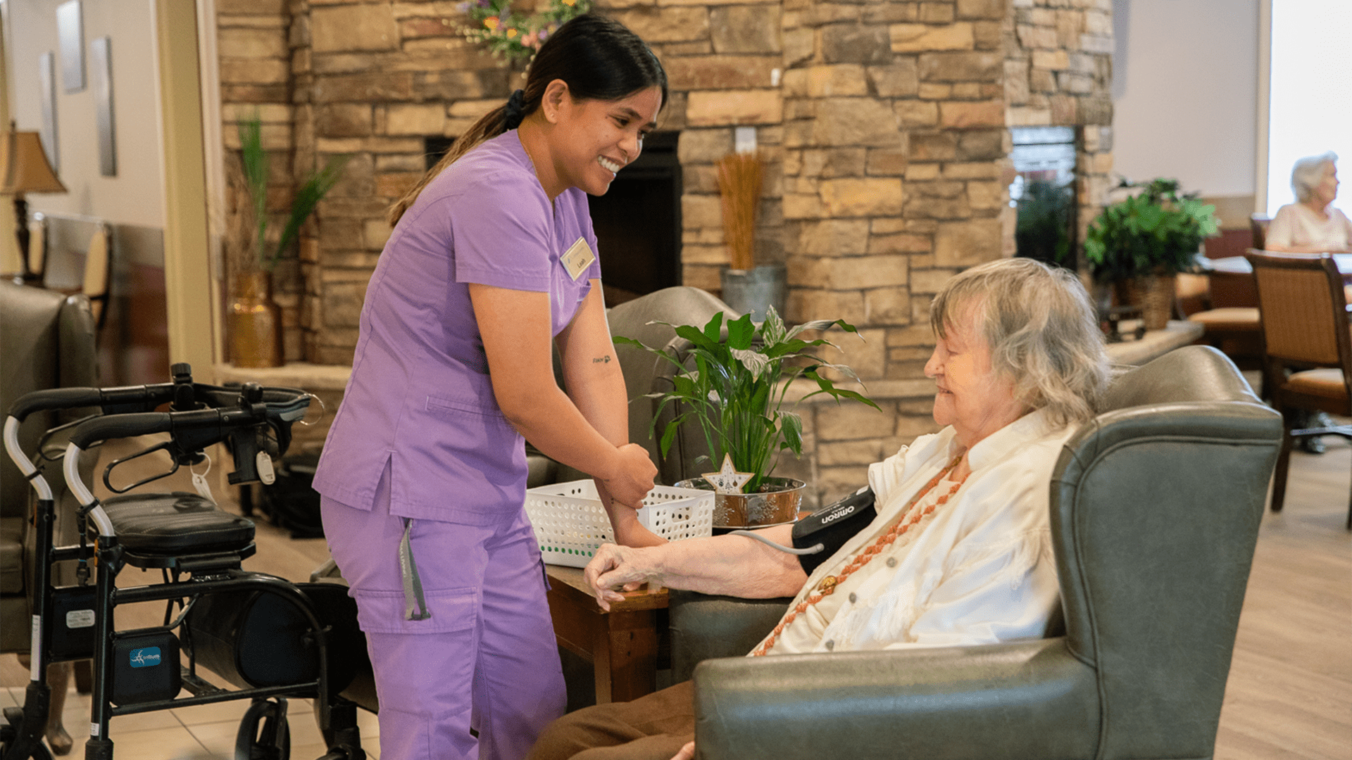 Nurse in purple scrubs helping a senior sitting in a chair